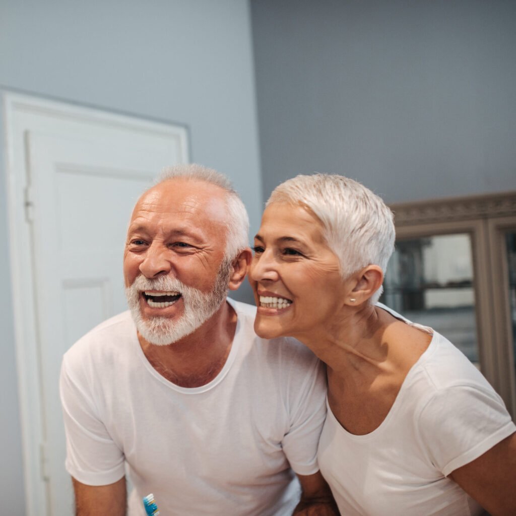 older couple smiling in bathroom mirror admiring their new dental implants
