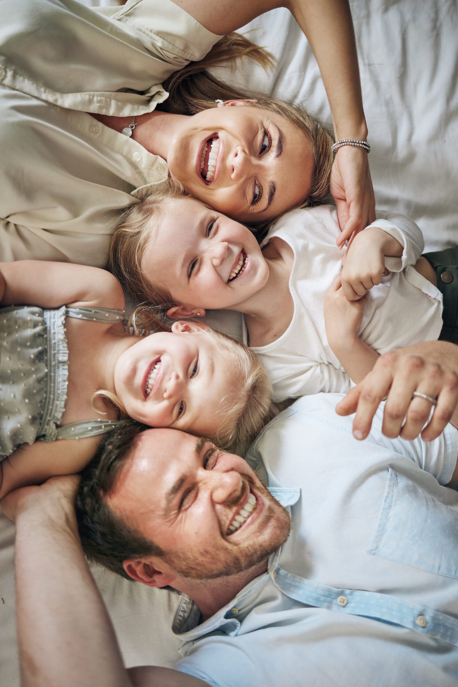 portrait of a family of four smiling and laughing laying down on a bed together