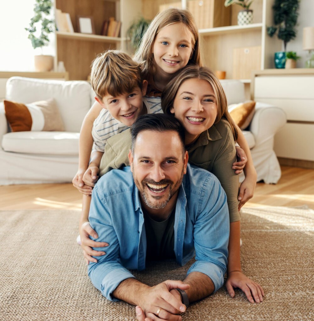 Cheerful father lying on floor with three smiling children piled on his back, embracing and enjoying family time at home