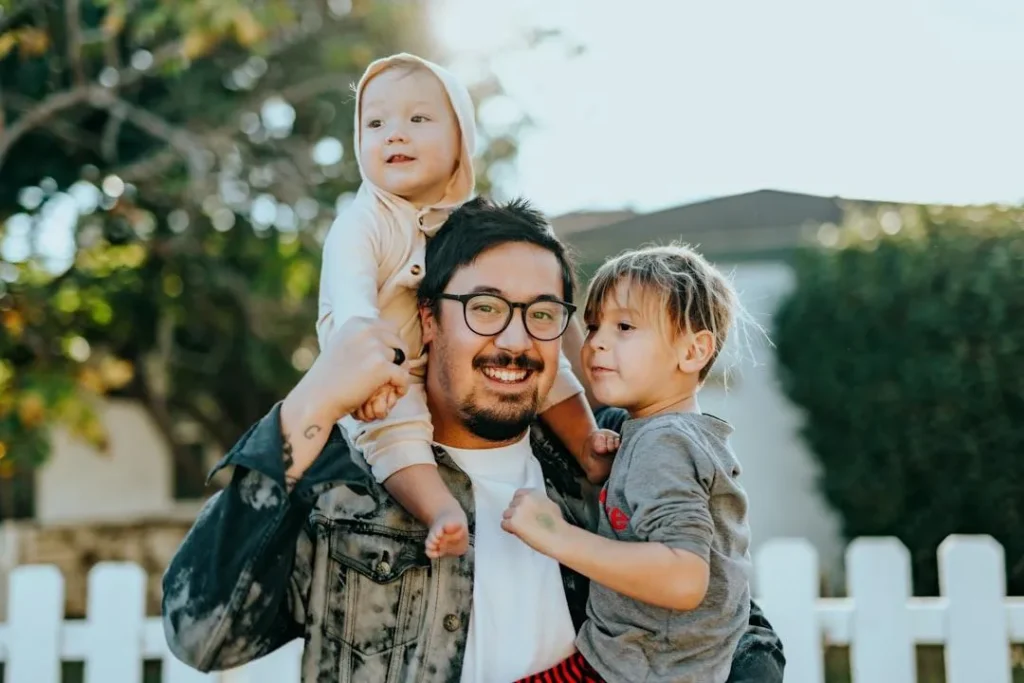 Father with his two babies posing for a portrait outside while holing one child and the other is on his shoulders