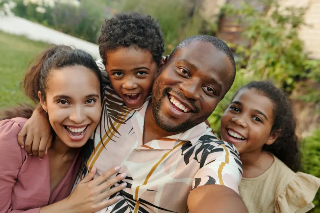 family of 4 outside smiling at the camera while the dad takes a selfie of them