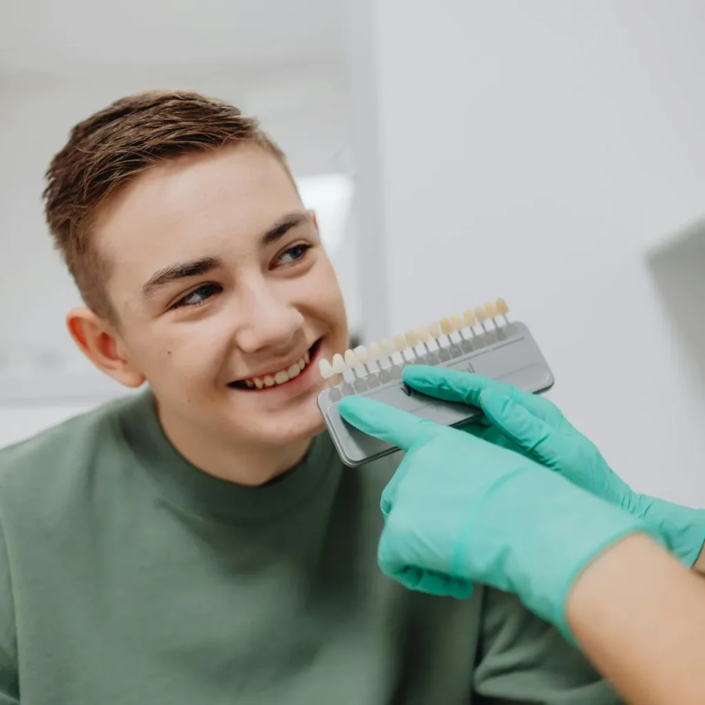 boy in chair at dental office smiling with teeth whitening scale being compared to his teeth