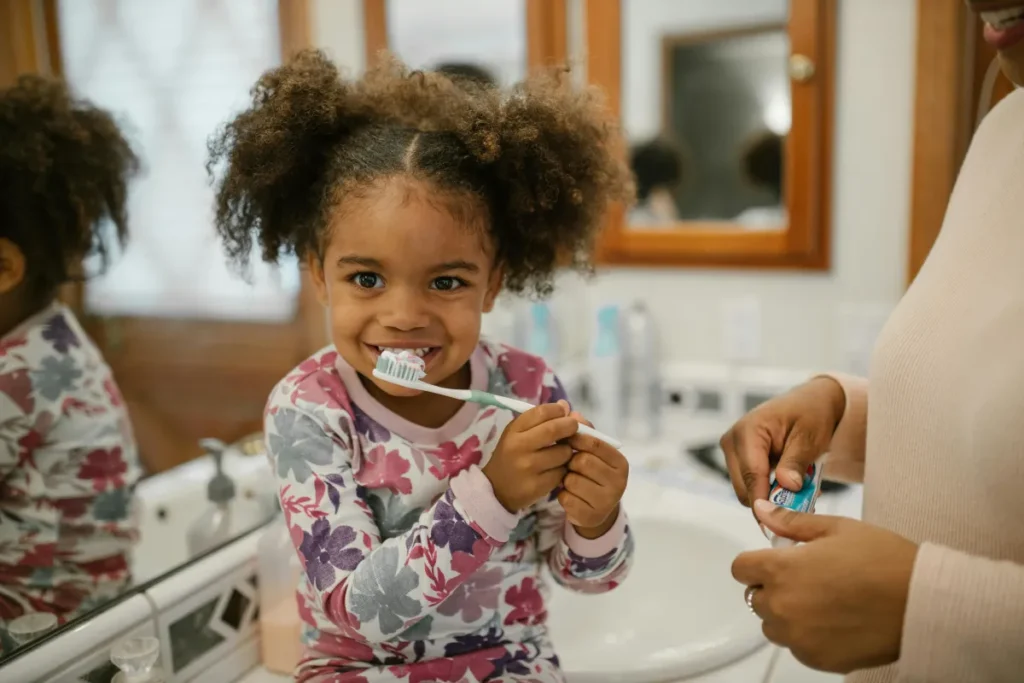 girl sitting on bathroom counter posing for portrait while she is learning how to brush her teeth