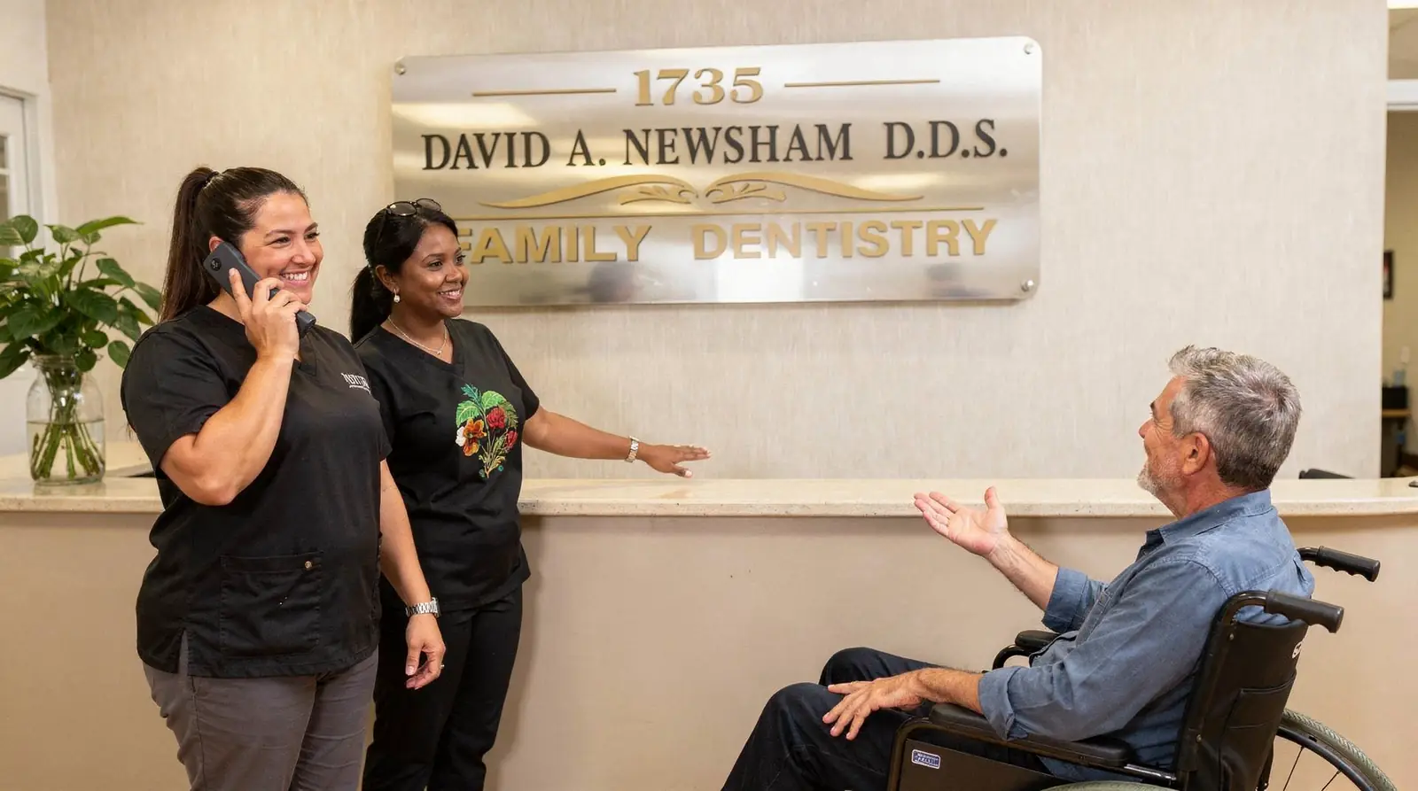 David A. Newsham DDS office reception with staff assisting a patient in a wheelchair, discussing